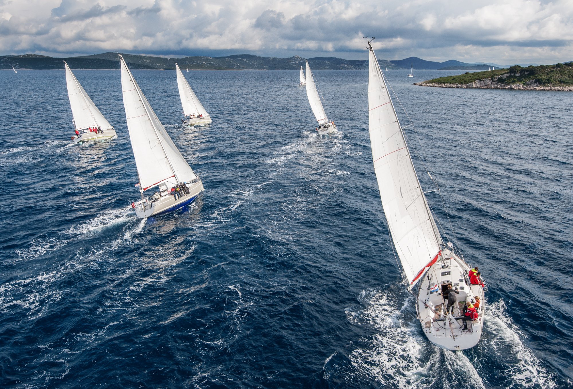 Aerial view of a sailing fleet reaching along a coastline during a regatta